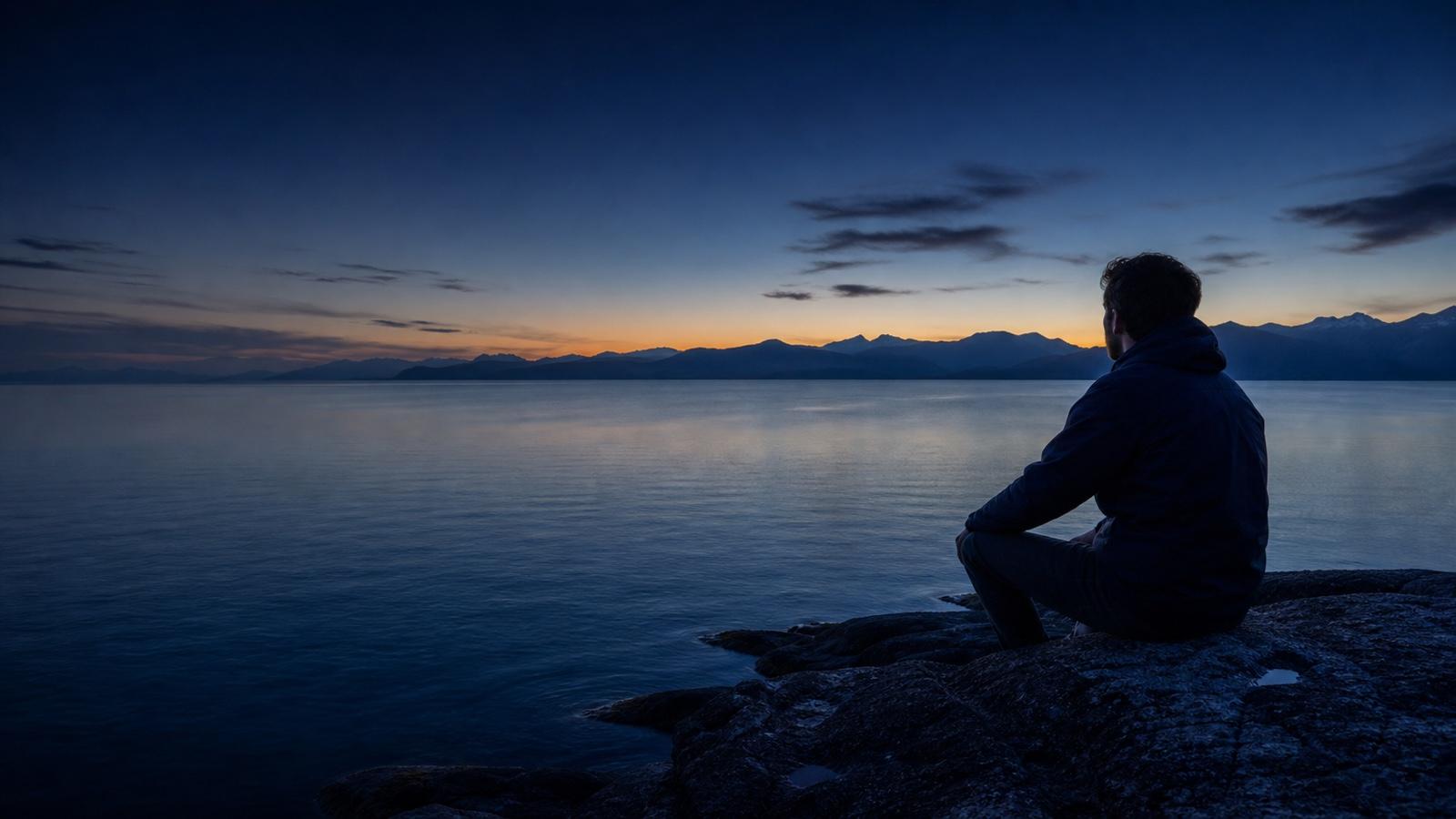 A traveler looking across calm water toward distant mountains.